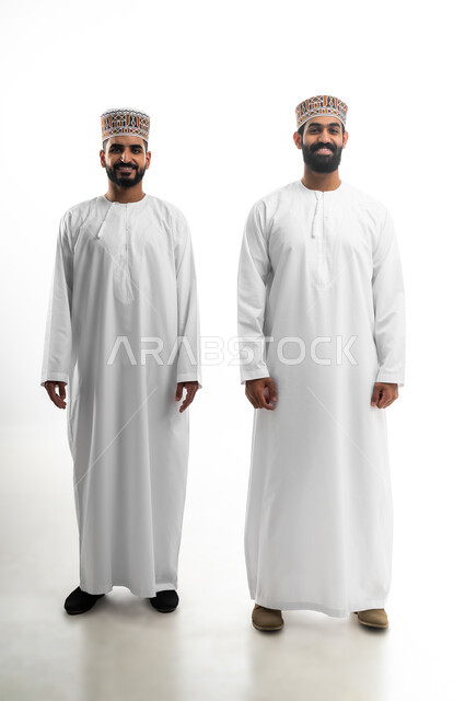 مفهوم الاهتمام بالمظهر الخارجي والأناقة والنظافة الشخصية، النظر للكاميرا بتعابير السعادة والسرور، بورتريه لشابان عربيان خليجيان عمانيان يرتديان الدشداشة والكمه تظهر عليهما علامات الفرح، الجسم بالطول الكامل، خلفية بيضاء