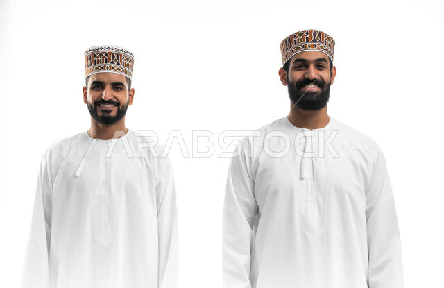 مفهوم الاهتمام بالمظهر الخارجي والأناقة والنظافة الشخصية، النظر للكاميرا بتعابير السعادة والسرور، بورتريه مقرب لشابان عربيان خليجيان عمانيان يرتديان الدشداشة والكمه تظهر عليهما علامات الفرح، خلفية بيضاء