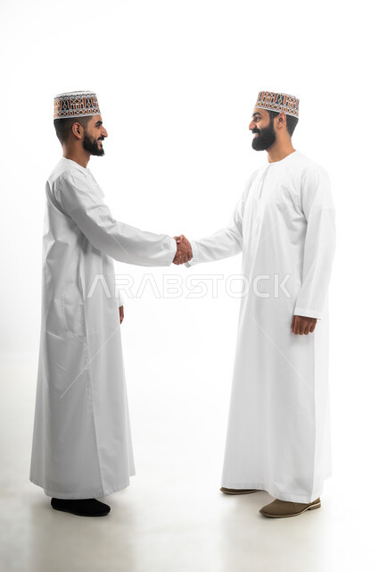 حركة يدين تدل على المصافحة و رد السلام وإلقاء التحية، المقابلة بهدف العمل، بورتريه لشابان عربيان خليجيان عمانيان يرتديان الدشداشة والكمه يتقابلان بتعابير الفرح والسرور، اللطف والرقي في التعامل مع الآخرين، خلفية بيضاء
