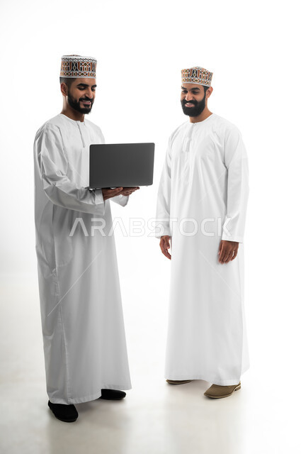 مفهوم الحوار والمناقشة في شؤون العمل، المشاركة في إنهاء الأعمال، مفهوم الجد والاجتهاد، بورتريه لشابان عربيان خليجيان عمانيان يرتديان الدشداشة والكمه تظهر عليهما علامات الفرح والسرور، استخدام التقنيات الحديثة لإنجاز المهام، خلفية بيضاء