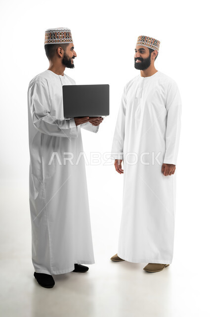 المشاركة في إنهاء الأعمال، مفهوم الجد والاجتهاد، بورتريه لشابان عربيان خليجيان عمانيان يرتديان الدشداشة والكمه تظهر عليهما علامات الفرح والسرور، النقاش والحوار في شؤون العمل، استخدام التقنيات الحديثة لإنجاز المهام، خلفية بيضاء