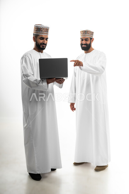 المشاركة في إنهاء الأعمال، مفهوم الجد والاجتهاد، بورتريه لشابان عربيان خليجيان عمانيان يرتديان الدشداشة والكمه تظهر عليهما علامات الفرح والسرور، النقاش والحوار في شؤون العمل، استخدام التقنيات الحديثة لإنجاز المهام، خلفية بيضاء