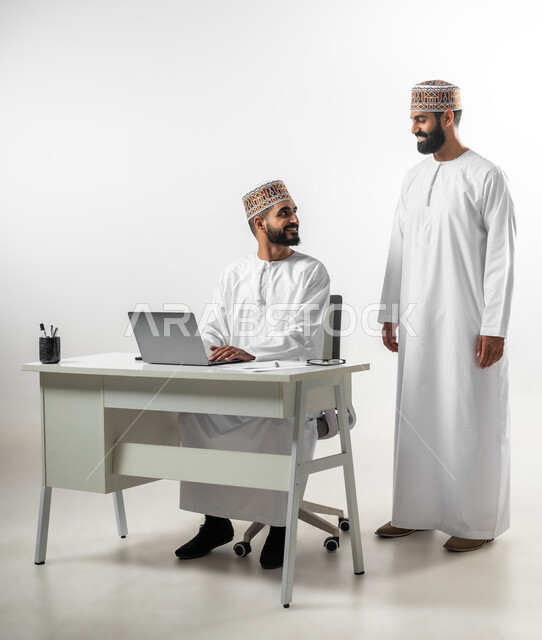 أجواء عمل وإنجاز مهام، بورتريه لشابان عربيان خليجيان عمانيان يرتديان الدشداشة والكمه تظهر عليهما علامات الفرح والسرور، اللطف والرقي في التعامل مع الموظفين، ايماءات السعادة والانبساط، خلفية بيضاء