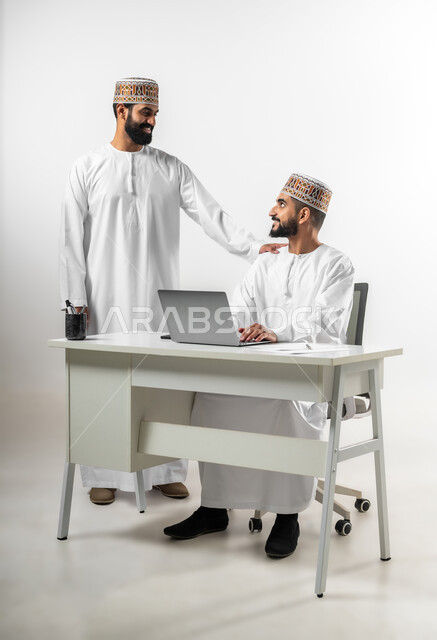 أجواء عمل وإنجاز مهام، بورتريه لشابان عربيان خليجيان عمانيان يرتديان الدشداشة والكمه تظهر عليهما علامات الفرح والسرور، اللطف والرقي في التعامل مع الموظفين، ايماءات السعادة والانبساط، خلفية بيضاء