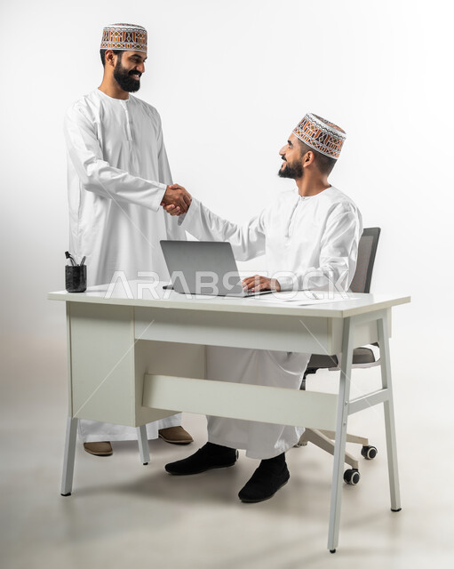 حسن الاستقبال و الابتسامة في وجه الآخرين والرقي في المعاملة، المصافحة ورد السلام، بورتريه لشابان عربيان عمانيان يرتدي كل منهما دشداشة وكمه يقابلان بعضهما بايماءات السرور، خلفية بيضاء
