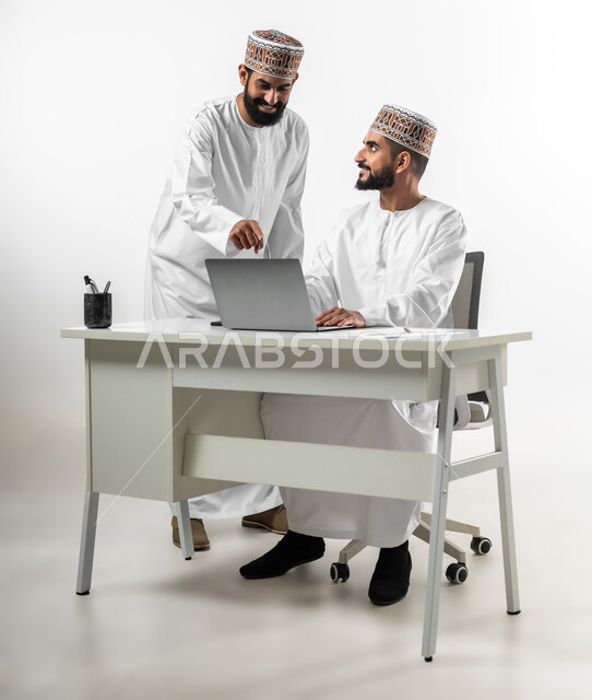 إعطاء التعليمات وشرح المهام، الرقي واللطف في التعامل بين الموظفين، بورتريه لشابان عربيان خليجيان عمانيان يرتديان الدشداشة والكمه يقومان بالمشاركة في العمل، تعابير وجه تدل على الفرح والسرور، خلفية بيضاء