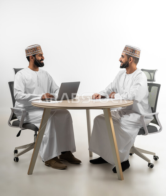 الدردشة والمشاركة في إنجاز المهام المطلوبة، الصحبة وتبادل الأحاديث والخبرات، بورتريه لشابان عربيان خليجيان عمانيان يرتديان الدشداشة والكمه تظهر عليهما علامات الفرح والسرور، استخدم التقنيات الحديثة لإنهاء الأعمال، خلفية بيضاء