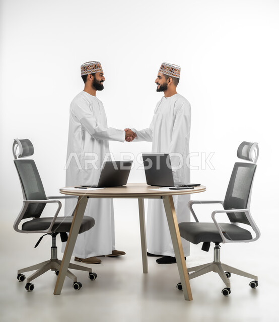 حركة يدين تدل على السلام وإلقاء التحية، المقابلة بهدف العمل، بورتريه لشابان عربيان خليجيان عمانيان يرتديان الدشداشة والكمه يتقابلان بتعابير الفرح والسرور، اللطف والرقي في التعامل مع الآخرين، خلفية بيضاء
