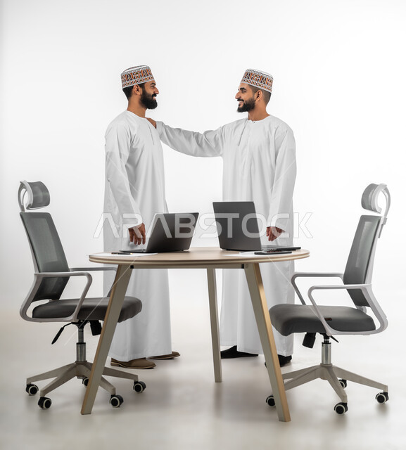 الدردشة مع الأصدقاء، الرقي في التعامل وتبادل الأحاديث، بورتريه لشابان عربيان خليجيان عمانيان يرتديان الدشداشة والكمه تظهر عليهما علامات الفرح والسرور، الجسم بالطول الكامل، خلفية بيضاء