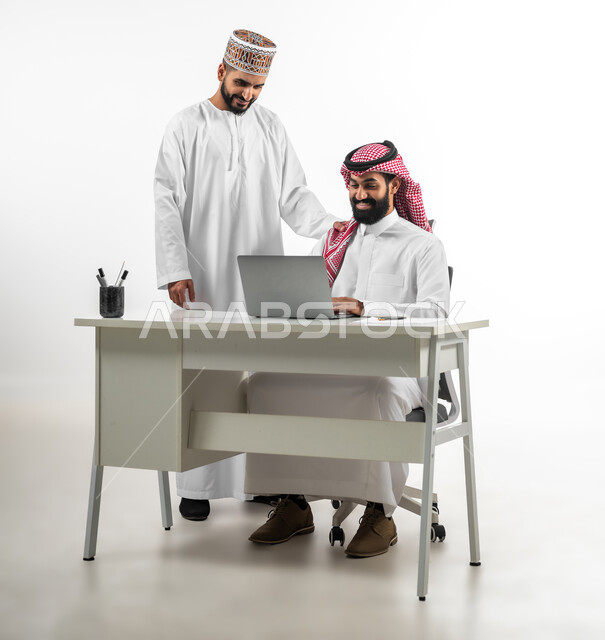 أجواء عمل وإنجاز مهام، بورتريه لشاب عربي عماني يرتدي الدشداشة والكمه يقوم بشرح طبيعة الأعمال لرجل سعودي يلبس الشماخ، اللطف والرقي في التعامل مع الموظفين، ايماءات السعادة والسرور، خلفية بيضاء