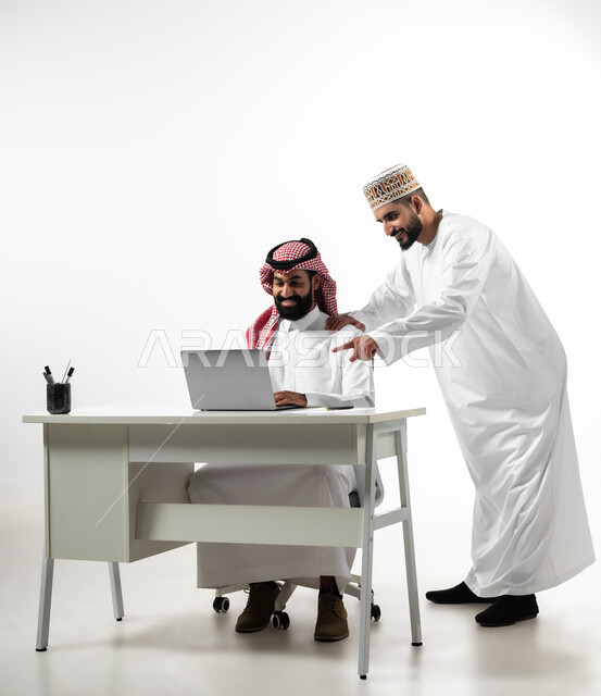 أجواء عمل وإنجاز مهام، بورتريه لشاب عربي عماني يرتدي الدشداشة والكمه يقوم بشرح طبيعة الأعمال لرجل سعودي يلبس الشماخ، اللطف والرقي في التعامل مع الموظفين، ايماءات السعادة والسرور، خلفية بيضاء