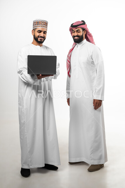 المشاركة في إنجاز الأعمال، مفهوم العمل والاجتهاد، بورتريه لشاب عماني يرتدي الدشداشة والكمه وآخر سعودي تظهر عليهما علامات الفرح والسرور، الجسم بالطول الكامل، تبادل الثقافات بين الدول العربية، خلفية بيضاء