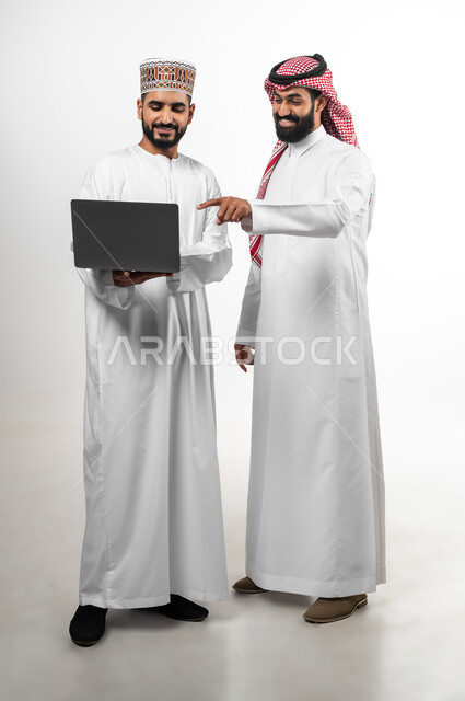 المشاركة في إنجاز الأعمال، مفهوم العمل والاجتهاد، بورتريه لشاب عماني يرتدي الدشداشة والكمه وآخر سعودي تظهر عليهما علامات الفرح والسرور، الجسم بالطول الكامل، تبادل الثقافات بين الدول العربية، خلفية بيضاء