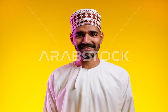 مفهوم الاناقة و الاهتمام بالمظهر الخارجي, بورتريه  لشاب عربي خليجي عماني يرتدي الدشداشة و الكمه يقف وينظر بإيماءات السعادة و السرور, تعابير السير و المشي للذهاب الى مكان ما, الوقوف والنظر الى الامام، صوره مقربه، خلفيه برتقاليه