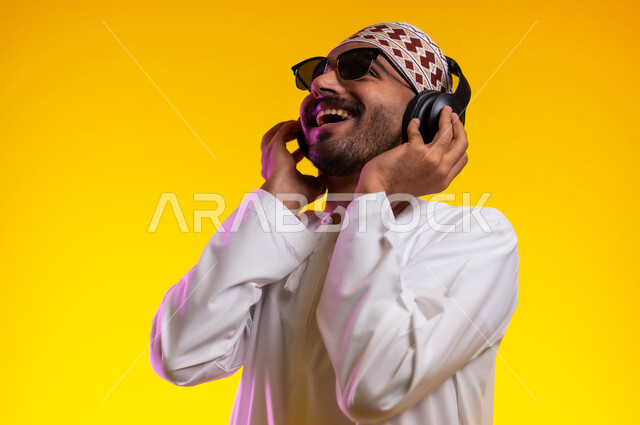 Artistic singing talents, gestures and expressions to blend in with the song, a portrait of an Arab Gulf Omani man wearing a dishdasha and a sleeve listening to music through headphones, gestures indicating listening and listening to songs using a headphone, interacting with musical melodies, a yellow background.