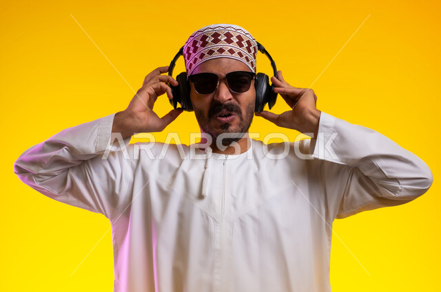 مواهب غنائية فنية، إيماءات وتعابير الاندماج مع الأغنية، بورتريه لرجل عربي خليجي عماني يرتدي الدشداشه والكمه يستمع الى الموسيقى من خلال سماعه الرأس، ايماءات تدل على الانصات والإستماع للأغاني بإستخدام الهيدفون، التفاعل مع الانغام الموسيقية، خلفية صفراء