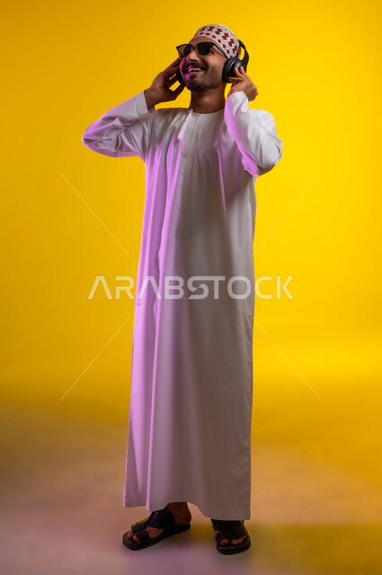 مواهب غنائية فنية، إيماءات وتعابير الاندماج مع الأغنية، بورتريه لرجل عربي خليجي عماني يرتدي الدشداشه والكمه يستمع الى الموسيقى من خلال سماعه الرأس، ايماءات تدل على الانصات والإستماع للأغاني بإستخدام الهيدفون، التفاعل مع الانغام الموسيقية، خلفية صفراء