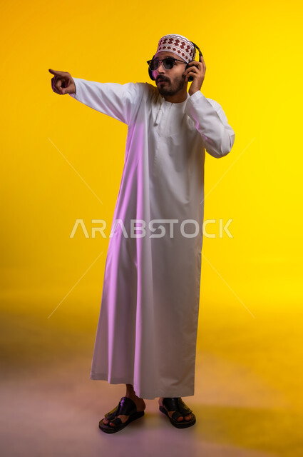 Artistic singing talents, gestures and expressions to blend in with the song, a portrait of an Arab Gulf Omani man wearing a dishdasha and a sleeve listening to music through headphones, gestures indicating listening and listening to songs using a headphone, interacting with musical melodies, a yellow background.