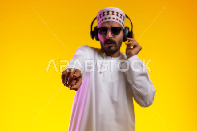 مواهب غنائية فنية، إيماءات وتعابير الاندماج مع الأغنية، بورتريه لرجل عربي خليجي عماني يرتدي الدشداشه والكمه يستمع الى الموسيقى من خلال سماعه الرأس، ايماءات تدل على الانصات والإستماع للأغاني بإستخدام الهيدفون، التفاعل مع الانغام الموسيقية، خلفية صفراء