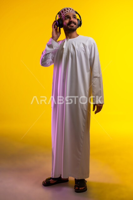 مواهب غنائية فنية، إيماءات وتعابير الاندماج مع الأغنية، بورتريه لرجل عربي خليجي عماني يرتدي الدشداشه والكمه يستمع الى الموسيقى من خلال سماعه الرأس، ايماءات تدل على الانصات والإستماع للأغاني بإستخدام الهيدفون، التفاعل مع الانغام الموسيقية، خلفية صفراء
