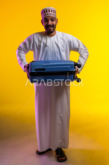 الاستعداد لوقت الرحلة، مفهوم السياحة والسفر، قضاء أوقات ممتعة في الإجازة, بورتريه لشاب عربي خليجي عماني يرتدي الدشداشة و الكمه يمسك حقيبة السفر بيده, النظر الى شيء ما بتعابير الحماس والسرور, خلفيه برتقاليه