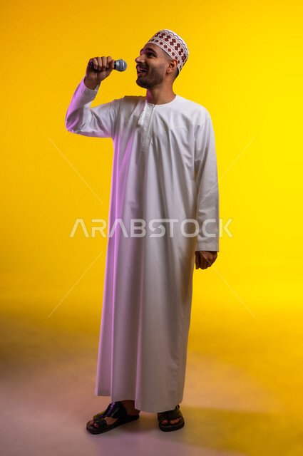 تقديم العروضات المسرحية، الاستمتاع بأداء المواهب الصوتية، بورتريه  لشاب عربي خليجي عماني يرتدي الدشداشه والكمه يمسك بيده المايكروفون، إيماءات وتعابير الاندماج والتفاعل مع الموسيقا، تسجيل مقطع صوتي غنائي، خلفيه برتقاليه