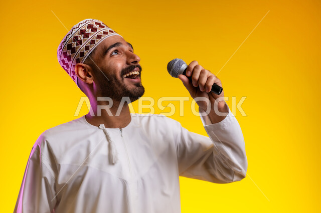 تقديم العروضات المسرحية، الاستمتاع بأداء المواهب الصوتية، بورتريه  لشاب عربي خليجي عماني يرتدي الدشداشه والكمه يمسك بيده المايكروفون، إيماءات وتعابير الاندماج والتفاعل مع الموسيقا، تسجيل مقطع صوتي غنائي، خلفيه برتقاليه
