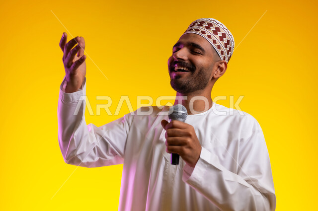 تقديم العروضات المسرحية، الاستمتاع بأداء المواهب الصوتية، بورتريه  لشاب عربي خليجي عماني يرتدي الدشداشه والكمه يمسك بيده المايكروفون، إيماءات وتعابير الاندماج والتفاعل مع الموسيقا، تسجيل مقطع صوتي غنائي، خلفيه برتقاليه
