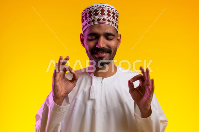 التعبير عن الجودة والإتقان, بورتريه لرجل عربي خليجي عماني يرتدي الدشداشة والكمه  يرفع يده للأعلى  بإيماءات الرضا والقبول والأعجاب, النظر الى الكاميرا بتعابير السرور, صورة الجسم بالطول الكامل, خلفية برتقاليه