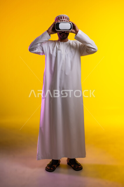 التطور التقني والتكنولوجي, المتعة و التسلية بالمشاهدة عبر نظارة الواقع الافتراضي، بورتريه لشاب عربي خليجي عماني يرتدي الدشداشه والكمه ينظر من خلال نظارات ثلاثية الأبعاد (الفي ار), الاندماج ومحاكاة العالم الخيالي والنظر الى الافلام الواقعيه، خلفيه برتقاليه
