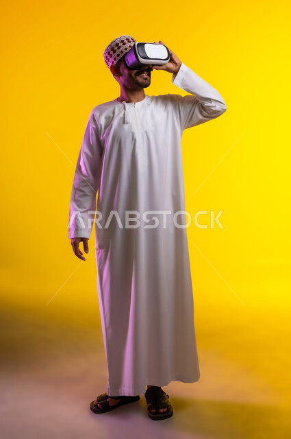 التطور التقني والتكنولوجي, المتعة و التسلية بالمشاهدة عبر نظارة الواقع الافتراضي، بورتريه لشاب عربي خليجي عماني يرتدي الدشداشه والكمه ينظر من خلال نظارات ثلاثية الأبعاد (الفي ار), الاندماج ومحاكاة العالم الخيالي والنظر الى الافلام الواقعيه، خلفيه برتقاليه