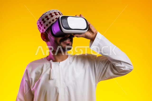 Technical and technological development, pleasure and entertainment in watching through virtual reality glasses, a portrait of an Arab Gulf Omani young man wearing a dishdasha and a sleeve, looking through 3D glasses (VR), merging and simulating the imaginary world and looking at realistic movies, orange background.