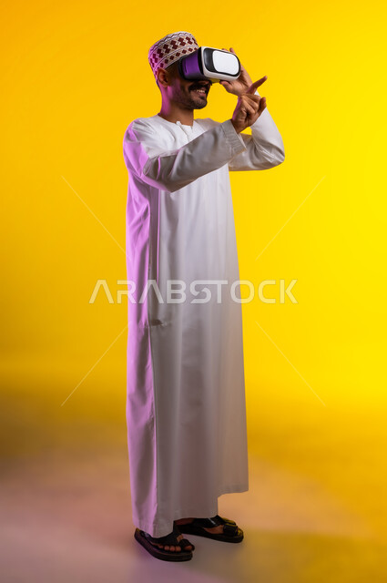 التطور التقني والتكنولوجي, المتعة و التسلية بالمشاهدة عبر نظارة الواقع الافتراضي، بورتريه لشاب عربي خليجي عماني يرتدي الدشداشه والكمه ينظر من خلال نظارات ثلاثية الأبعاد (الفي ار), الاندماج ومحاكاة العالم الخيالي والنظر الى الافلام الواقعيه، خلفيه برتقاليه