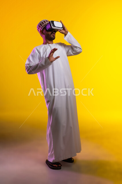 التطور التقني والتكنولوجي, المتعة و التسلية بالمشاهدة عبر نظارة الواقع الافتراضي، بورتريه لشاب عربي خليجي عماني يرتدي الدشداشه والكمه ينظر من خلال نظارات ثلاثية الأبعاد (الفي ار), الاندماج ومحاكاة العالم الخيالي والنظر الى الافلام الواقعيه، خلفيه برتقاليه