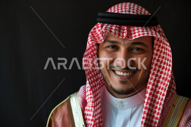 مفهوم الرجولة والأناقه، الاهتمام بالمظهر الخارجي، بورتريه مقرب لرجل عربي خليجي سعودي مبتسم يرتدي الشماغ والثوب التقليدي ينظر إلى الكاميرا بإيماءات السرور والفرح، خلفية سوداء