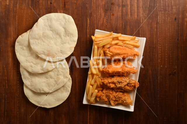 طبق لذيذ مكون من قطع من الدجاج المقلية الكرسبي اللذيذة المغلفة بالبقسماط ، مع بطاطا المقلية و الخبز الابيض العربي ، موضوع على سطح خشبي