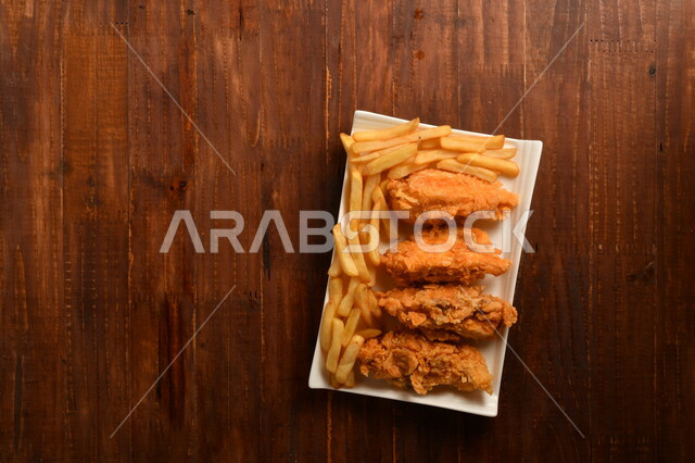 طبق لذيذ مكون من قطع من الدجاج المقلية الكرسبي اللذيذة المغلفة بالبقسماط ، مع بطاطا المقلية ، موضوع على سطح خشبي