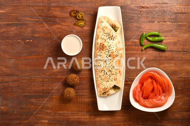 ساندويش فلافل لذيذ محشي داخل عجينة مخبوزة بمهارة ، بجانبه صوص الطحينة و اقراص الفلافل الشهية ، و طبق مقبلات من الطماطم ، طريقة تحضير الطعام ، مأكولات عربية شامية
