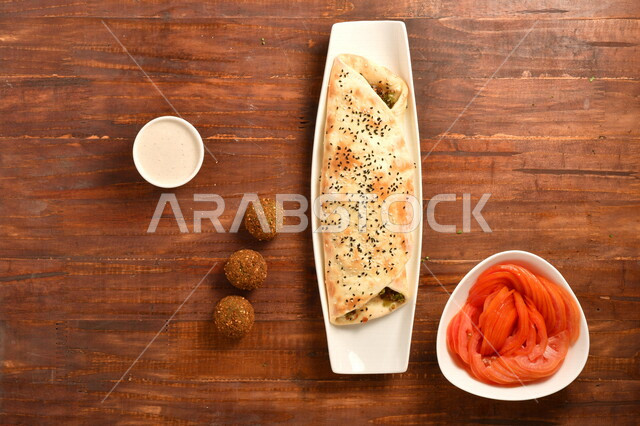 ساندويش فلافل لذيذ محشي داخل عجينة مخبوزة بمهارة ، بجانبه صوص الطحينة و اقراص الفلافل الشهية ، و طبق مقبلات من الطماطم ، طريقة تحضير الطعام ، مأكولات عربية شامية