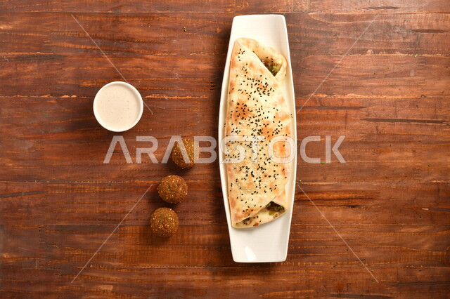 ساندويش فلافل لذيذ محشي داخل عجينة مخبوزة بمهارة ، بجانبه صوص الطحينة و اقراص الفلافل الشهية ، طريقة تحضير الطعام ، مأكولات عربية شامية