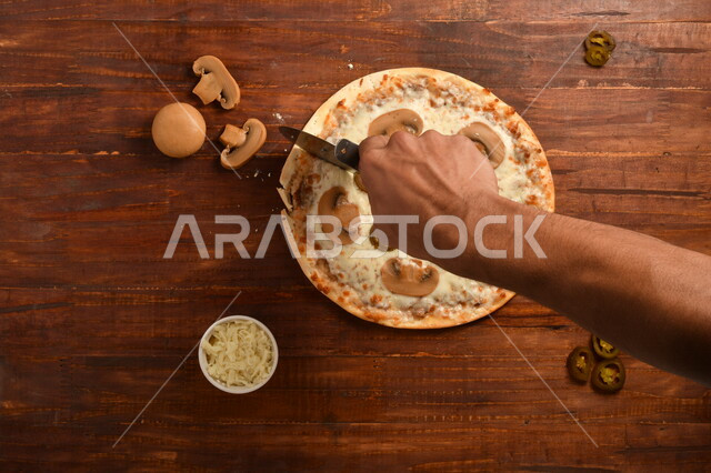 طبق فطور لذيذ و شهي  ، بيتزا دائرية الشكل مكونة من الفطر و الكثير من الجبنة السائلة ، مكونات عديدة متناثرة بجانب الطبق ، مخبوزات شهية ، سطح خشبي