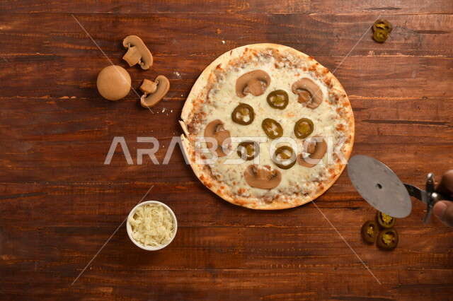 طبق فطور لذيذ و شهي  ، بيتزا دائرية الشكل مكونة من الفطر و الكثير من الجبنة السائلة ، مكونات عديدة متناثرة بجانب الطبق ، مخبوزات شهية ، سطح خشبي