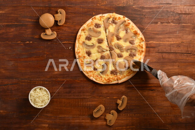 طبق فطور لذيذ و شهي  ، بيتزا دائرية الشكل مكونة من الفطر و الكثير من الجبنة السائلة ، مكونات عديدة متناثرة بجانب الطبق ، مخبوزات شهية ، سطح خشبي