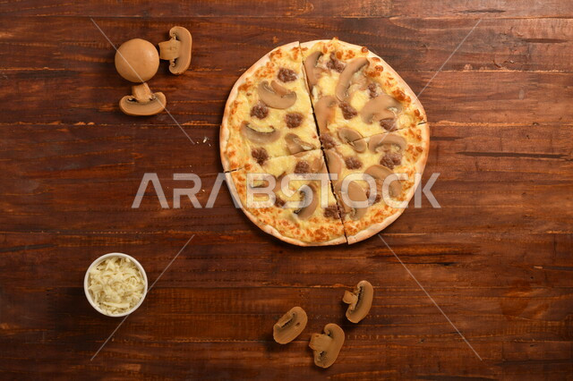 طبق فطور لذيذ و شهي  ، بيتزا دائرية الشكل مكونة من الفطر و الكثير من الجبنة السائلة ، مكونات عديدة متناثرة بجانب الطبق ، مخبوزات شهية ، سطح خشبي