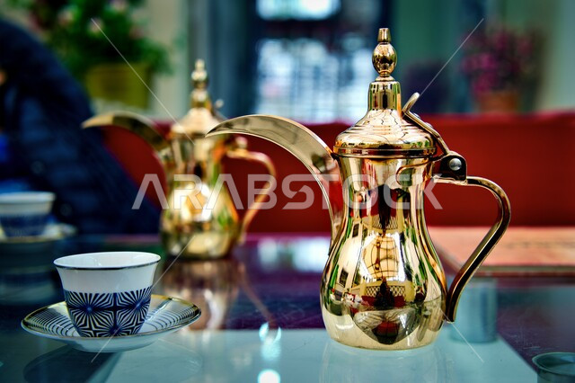 التقاليد والعادات الأصيلة المتوارثة من الأجداد, مفهوم الكرم وحسن استقبال الضيف في المملكة العربية السعودية, القهوة العربية الخليجية الفاخرة، دلة نحاسية ذهبية وبجانبها الفناجين, تقديم المشروبات الساخنة اللذيذة