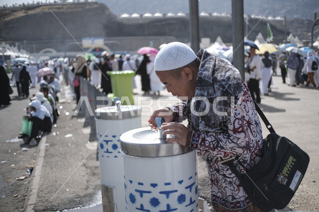 توفير الماء للحجاج بشكل مستمر في الأجواء الحارة، مقصد المسلمين من مختلف البلدان، موسم الحج في المملكة العربية السعودية، صورة مقربة لحاج يقوم بتعبئة المياه من أحد المبردات في أحد مناطق المشاعر المقدسة