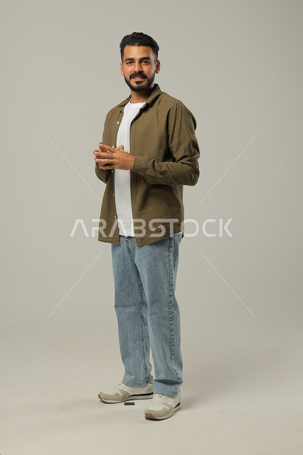 التأمل والتفكير و التخطيط للمستقبل، ايماءات التفكير بشيء ما، بورتريه لشاب وسيم عربي خليجي سعودي يرتدي الزي الكاجوال يقوم بملامسة اطراف اصابعه ببعضها بتعابير التمعن والتركيز لإيجاد حل لمشكلة ما، صورة لكامل الجسم، خلفية رمادية