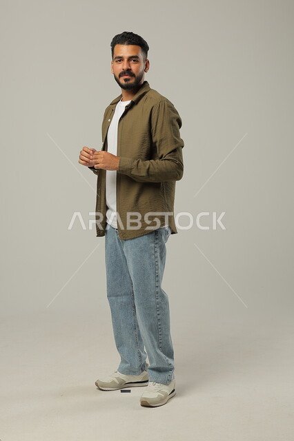 التأمل والتفكير و التخطيط للمستقبل، ايماءات التفكير بشيء ما، بورتريه لشاب وسيم عربي خليجي سعودي يرتدي الزي الكاجوال يقوم بملامسة اطراف اصابعه ببعضها بتعابير التمعن والتركيز لإيجاد حل لمشكلة ما، صورة لكامل الجسم، خلفية رمادية