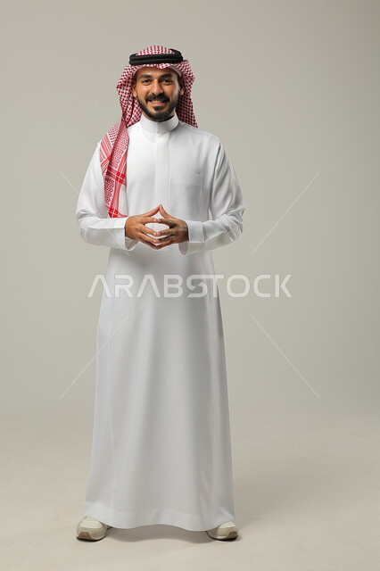 Finding a solution to a problem, thinking, contemplating, absent-mindedness and planning for the future, portrait of a young Saudi Arabian Gulf man wearing a traditional thobe and shemagh, touching his fingertips together, gestures of contemplation and concentration, full-length body image, gray background