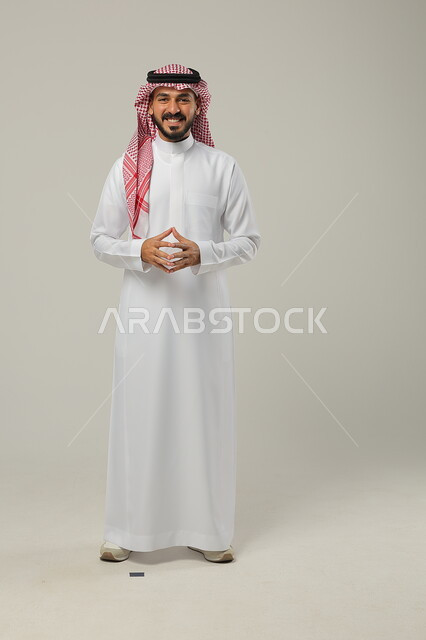 Finding a solution to a problem, thinking, contemplating, absent-mindedness and planning for the future, portrait of a young Saudi Arabian Gulf man wearing a traditional thobe and shemagh, touching his fingertips together, gestures of contemplation and concentration, full-length body image, gray background
